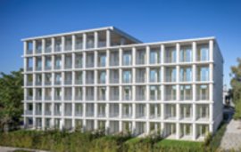Modernes weißes Mehrfamilienhaus mit regelmäßiger Fassade vor blauem Himmel und Grünflächen