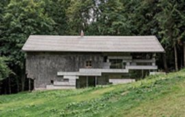 Betonbau im Wald: Ein modernes Haus mit Treppenstufen und Glasfassaden harmoniert mit der natürlichen Umgebung. (125 Zeichen)