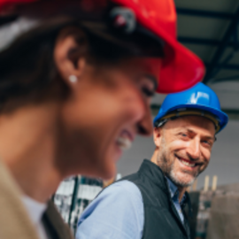 Zwei Bauarbeiter in Schutzhelmen lachen zusammen auf einer Baustelle im Fokus der Betonindustrie